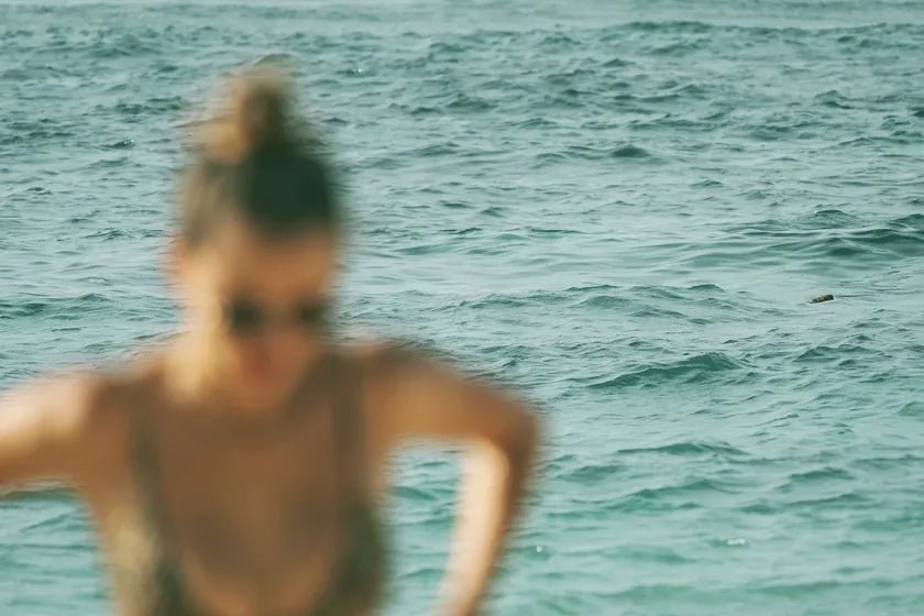 A woman with her hair twisted up off the neck, wading out of green summer sea