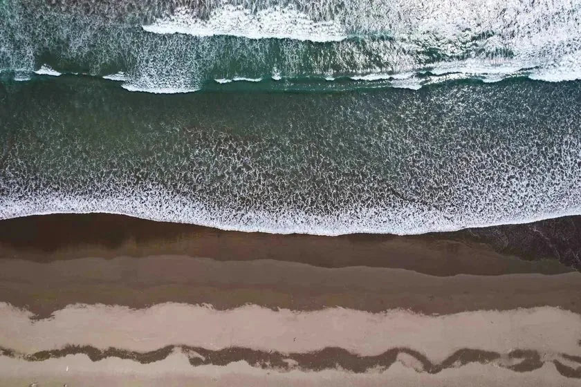 An aerial view of the tide meeting the shore in bands of sea, foam and wet sand