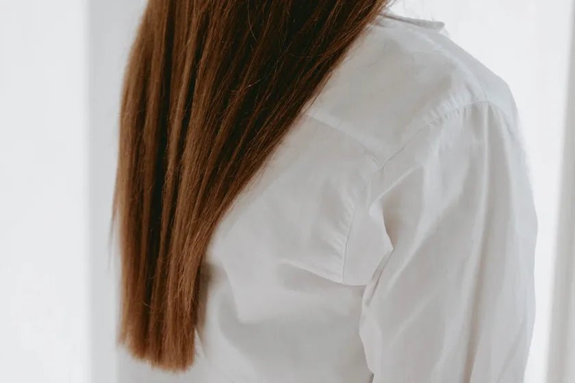 Straight brown hair falling over the shoulder of a crisp white shirt, seen from behind